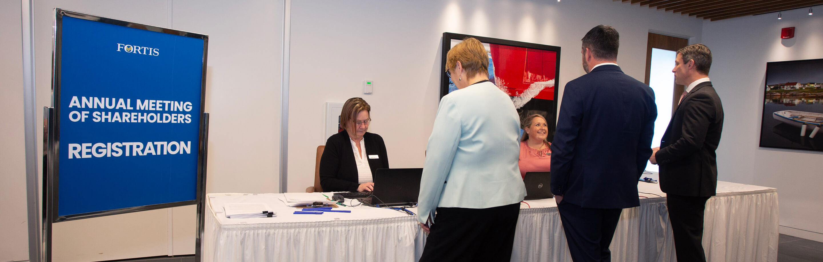 People stood at Fortis AGM registration desk with AGM signage