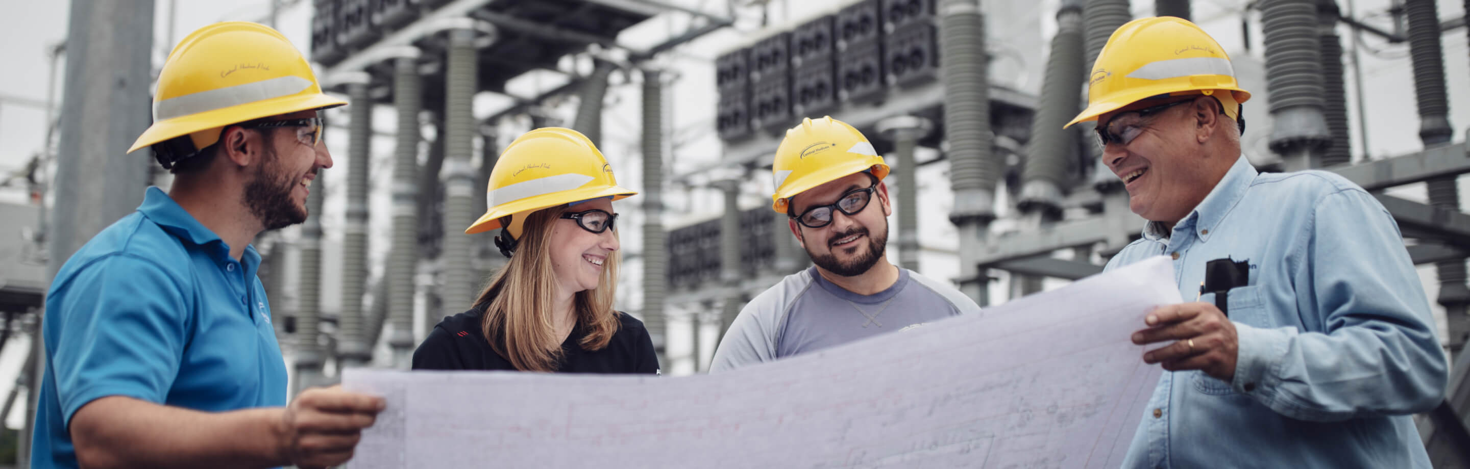 A woman and men wearing safety hats and viewing a large paper document