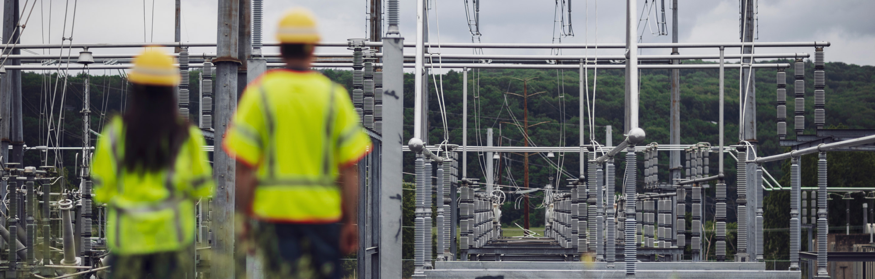 Woman and man wearing safety gear and standing in front of power transmission lines 