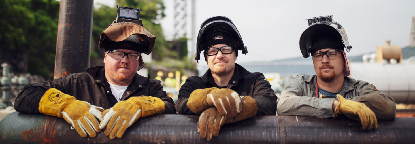 Three male employees in safety gear, resting on a pipe