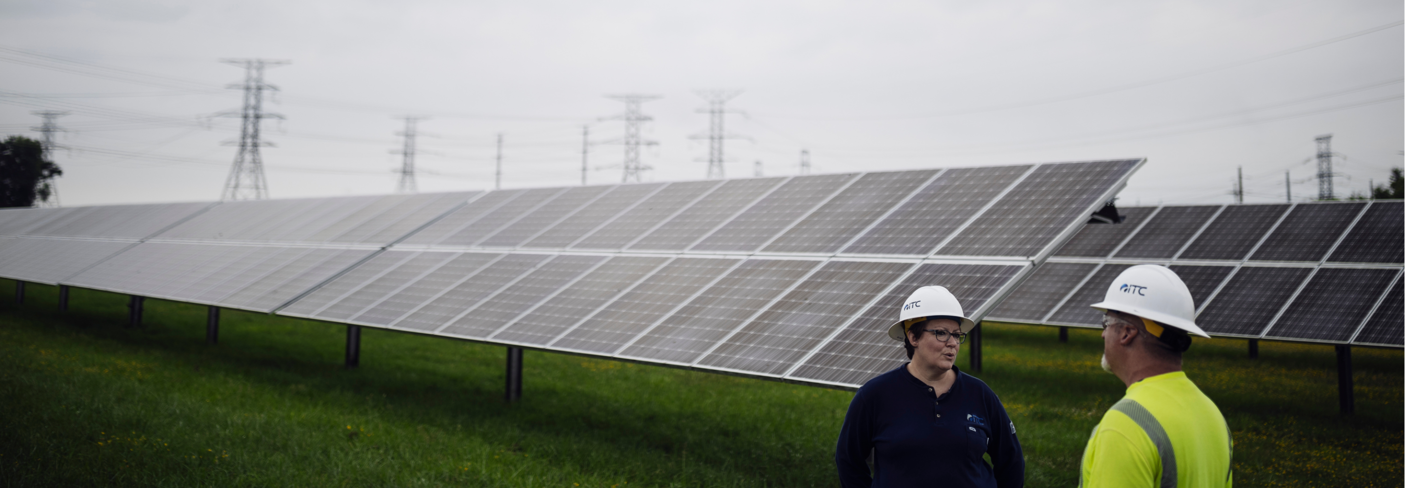 Woman and man wearing safety hats, talking in front of solar panels