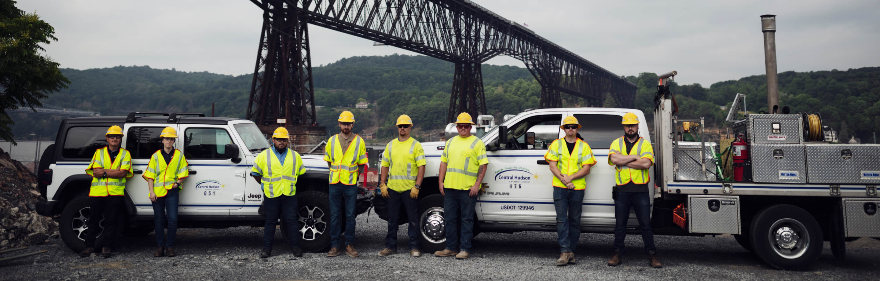 Several employees in front of work trucks, a river, and wooded background