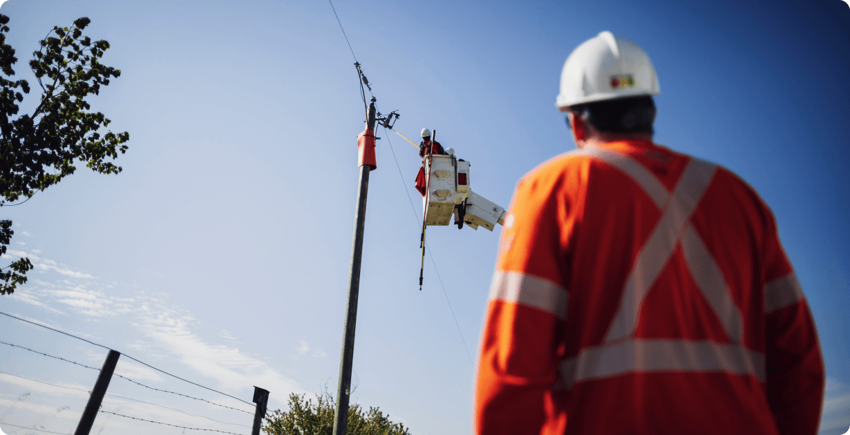 Man in safety gear spotting a lineman in a truck bucket repairing a power line