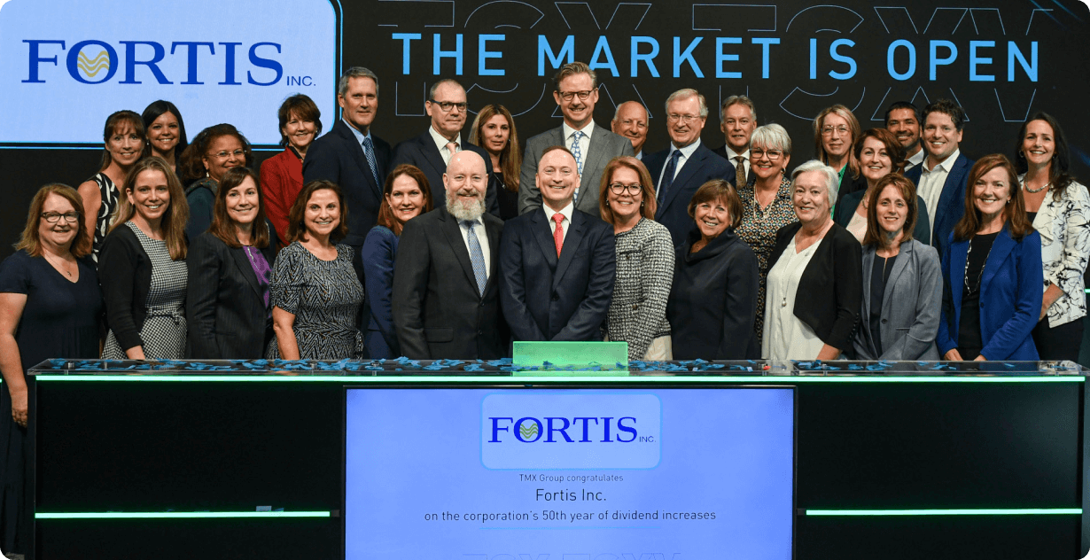 Fortis leaders celebrate in front of a stock exchange sign for Fortis